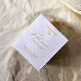 White product packaging with gold text on a textured beige background