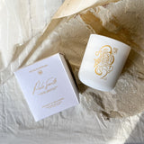 White candle and packaging with gold design on a textured stone surface
