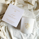 Spiritual White candle with gold logo on a textured beige fabric background