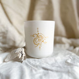 spiritual White Candle with gold design on a white surface with beige fabric in the background