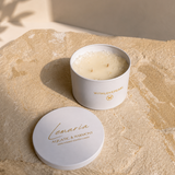 A white cylindrical candle tin with its lid placed beside it on a textured beige stone surface. The candle wax is visible, and the lid and tin are printed with the brand name 'Lemuria' and the scent 'Aquatic & Harmonic'.