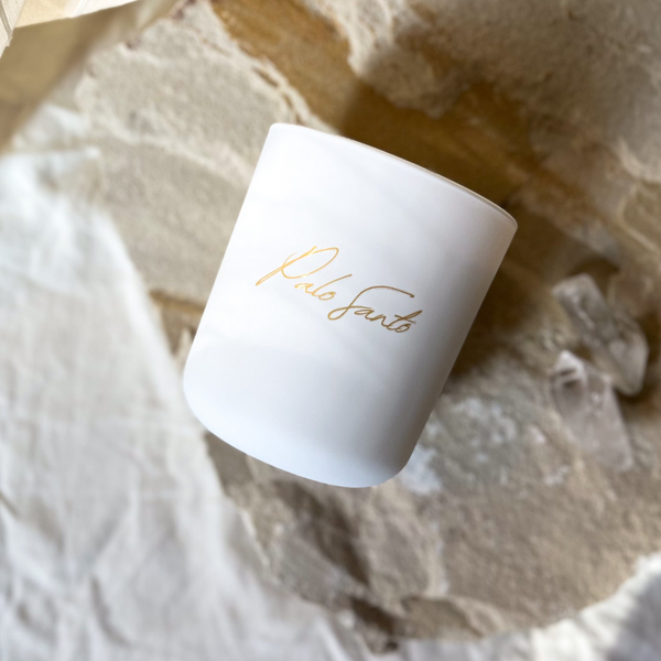 White candle with gold text on a textured white surface